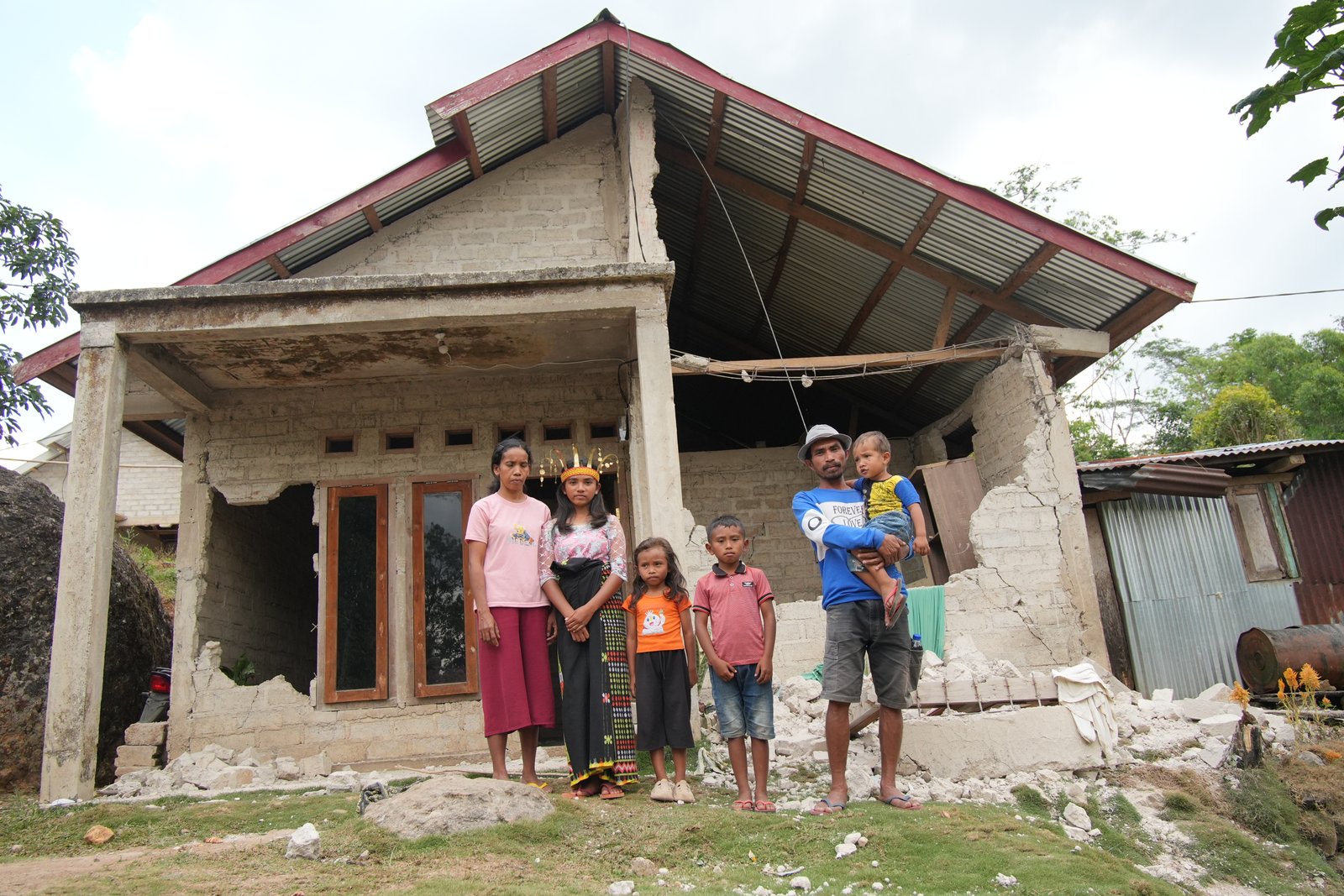 Prili and her family in front of their earthquake-damaged home